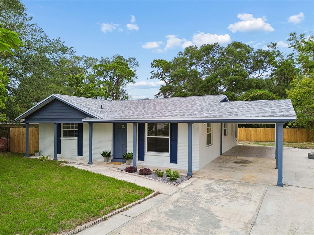 A single-story house with white brick, blue trim, and a side carport under a blue sky — 6532 S WEST SHORE CIRCLE, TAMPA, FL