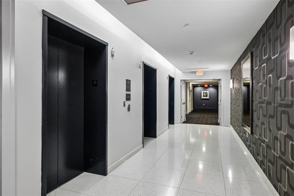 A hallway with white tile floors, black elevator doors, and a patterned accent wall — 260 S OSCEOLA AVENUE UNIT 1005, ORLANDO, FL