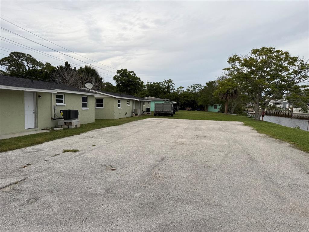A gravel parking area sits beside a light green building with a canal in the background — 7228 NEW YORK AVENUE, HUDSON, FL
