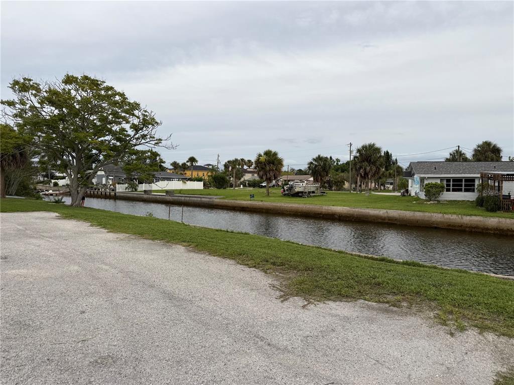 A canal separates a gravel parking area from a grassy lot with palm trees — 7228 NEW YORK AVENUE, HUDSON, FL