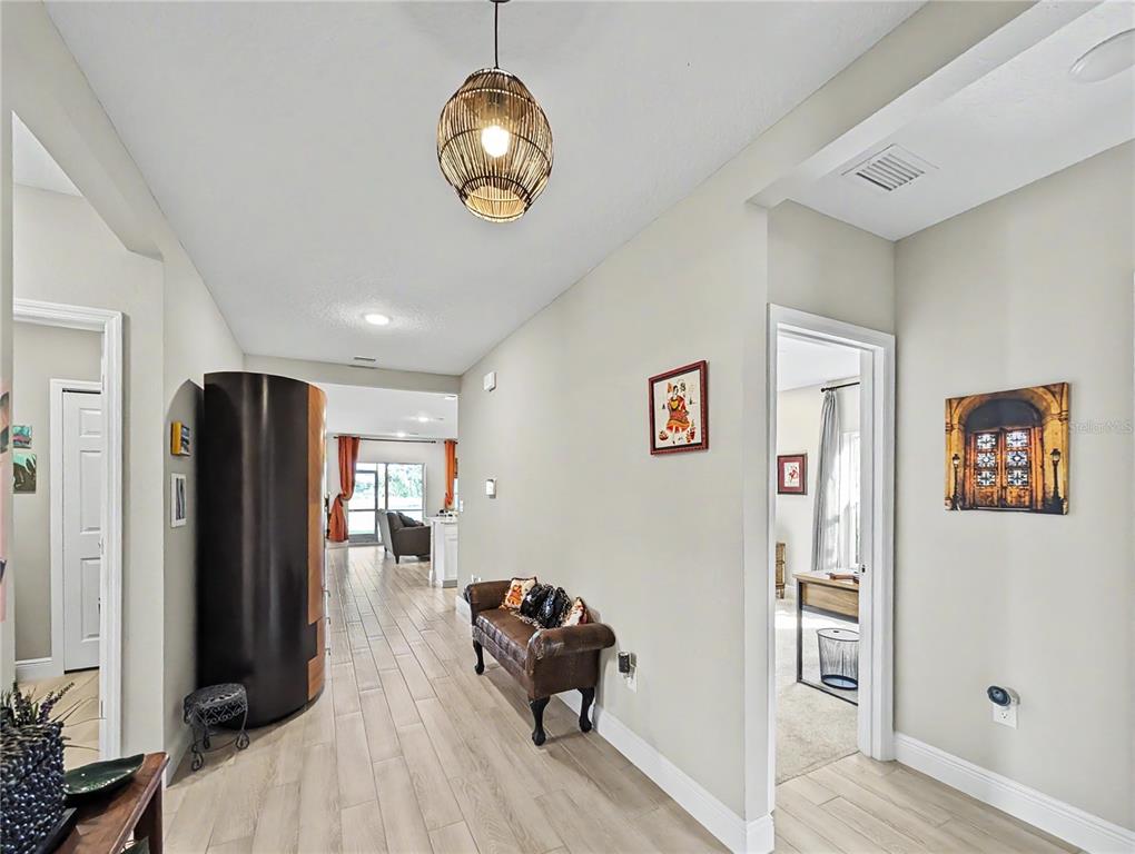 A hallway with light wood-look flooring leads to an open living area with a pendant light — 5220 BADINI WAY, PALMETTO, FL