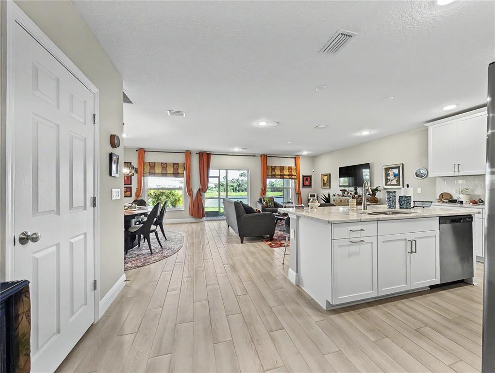An open-concept kitchen and living area features light wood-look tile flooring and white cabinetry — 5220 BADINI WAY, PALMETTO, FL