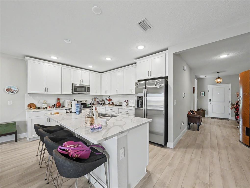 A modern kitchen features white cabinets, a marble-topped island with bar stools, and stainless appliances — 5220 BADINI WAY, PALMETTO, FL