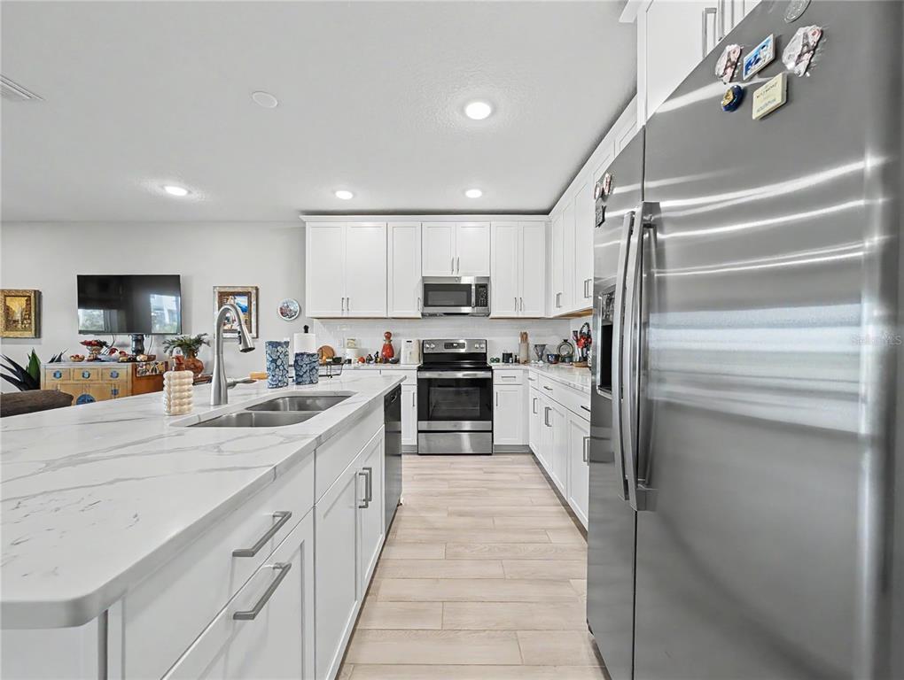 A modern kitchen features white cabinets, stainless steel appliances, and a large marble-topped island — 5220 BADINI WAY, PALMETTO, FL