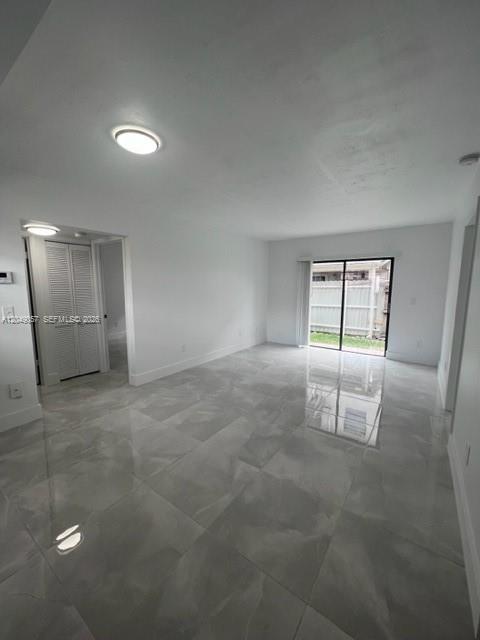 An empty room with white walls, gray tile flooring, and a sliding glass door to outside — HIALEAH, FL