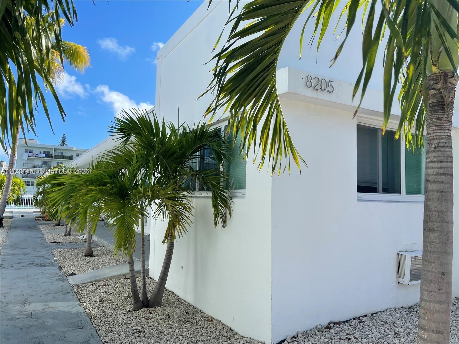 The exterior of a white building features palm trees, gravel landscaping, and a window unit — 8205 Crespi Blvd # 3, Miami Beach FL 33141, MIAMI BEACH, FL