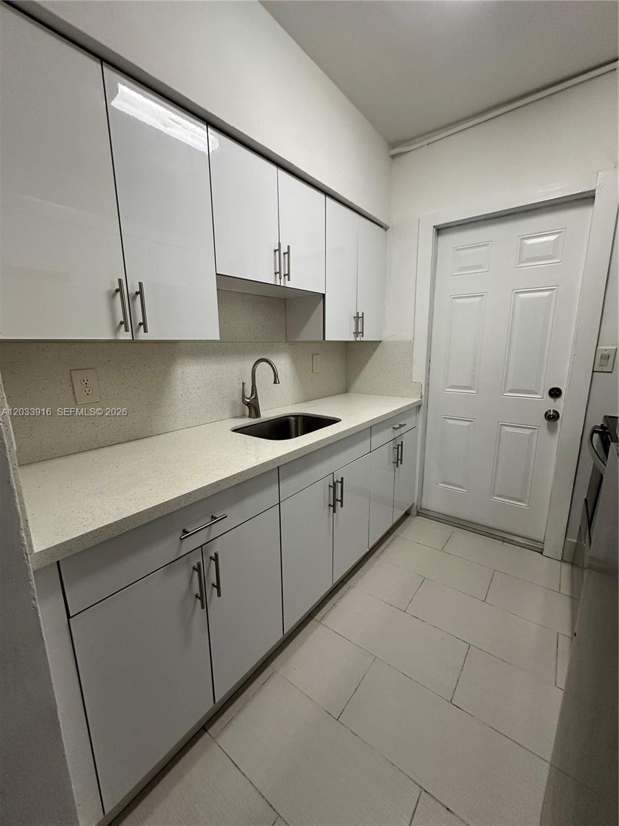 A small kitchen features white cabinets, light countertops, a sink, and a white door — 8205 Crespi Blvd # 3, Miami Beach FL 33141, MIAMI BEACH, FL