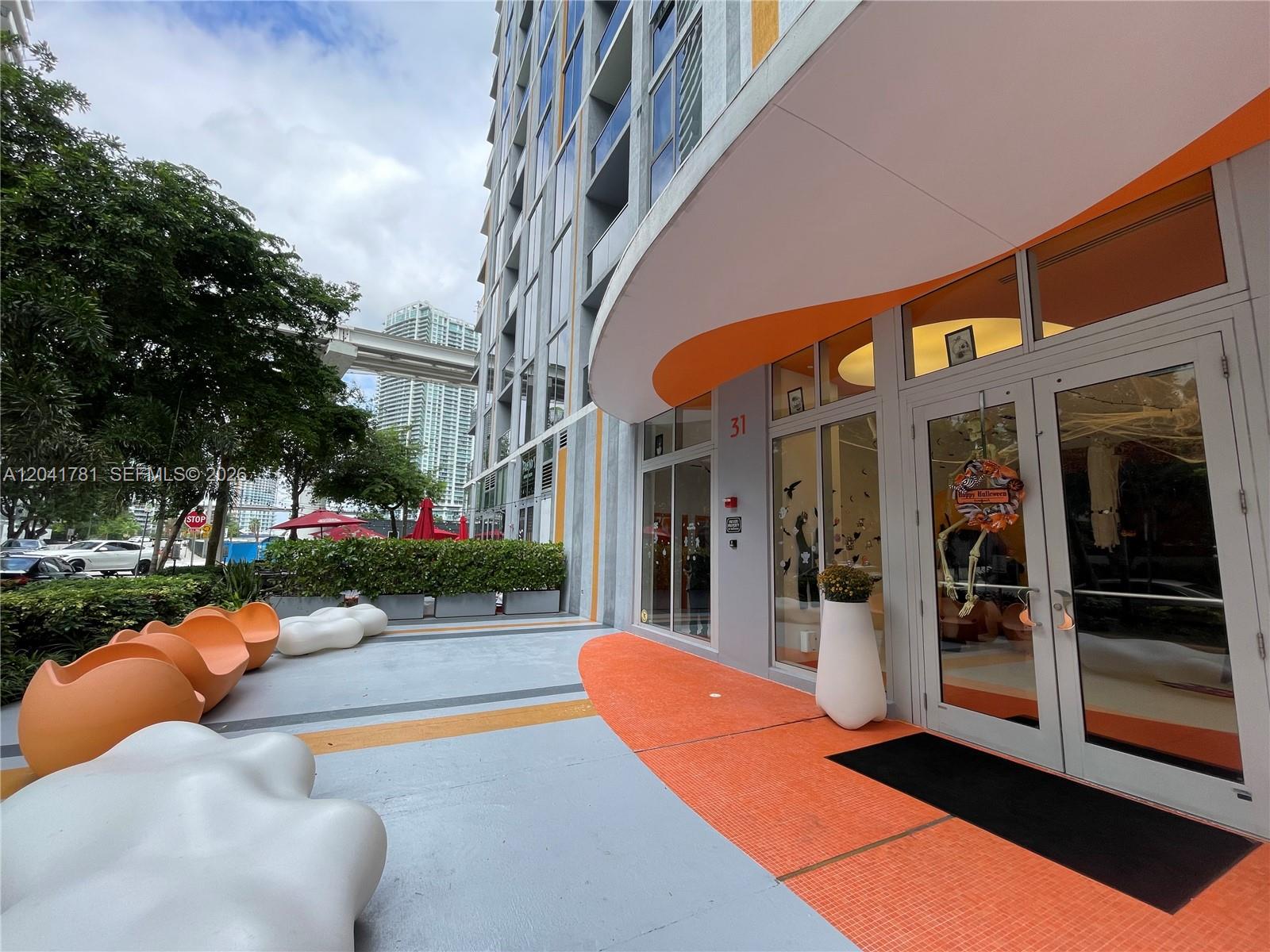 The exterior entrance of a modern building features orange accents, white seating, and glass doors — 31 SE 6th St # 2503, Miami FL 33131, MIAMI, FL