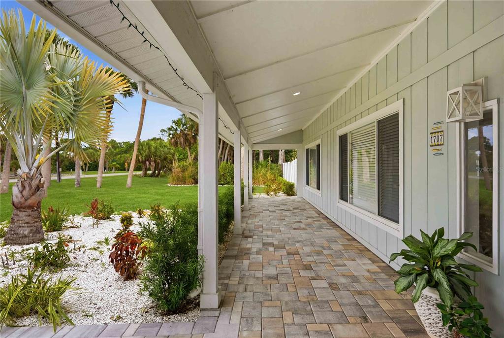 A covered porch with stone pavers, white columns, and light blue siding overlooks a grassy yard — 1707 BELVIDERE ROAD, ENGLEWOOD, FL