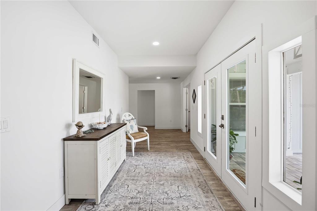 A bright entryway features white walls, wood-look flooring, a white console table, and glass doors — 1707 BELVIDERE ROAD, ENGLEWOOD, FL