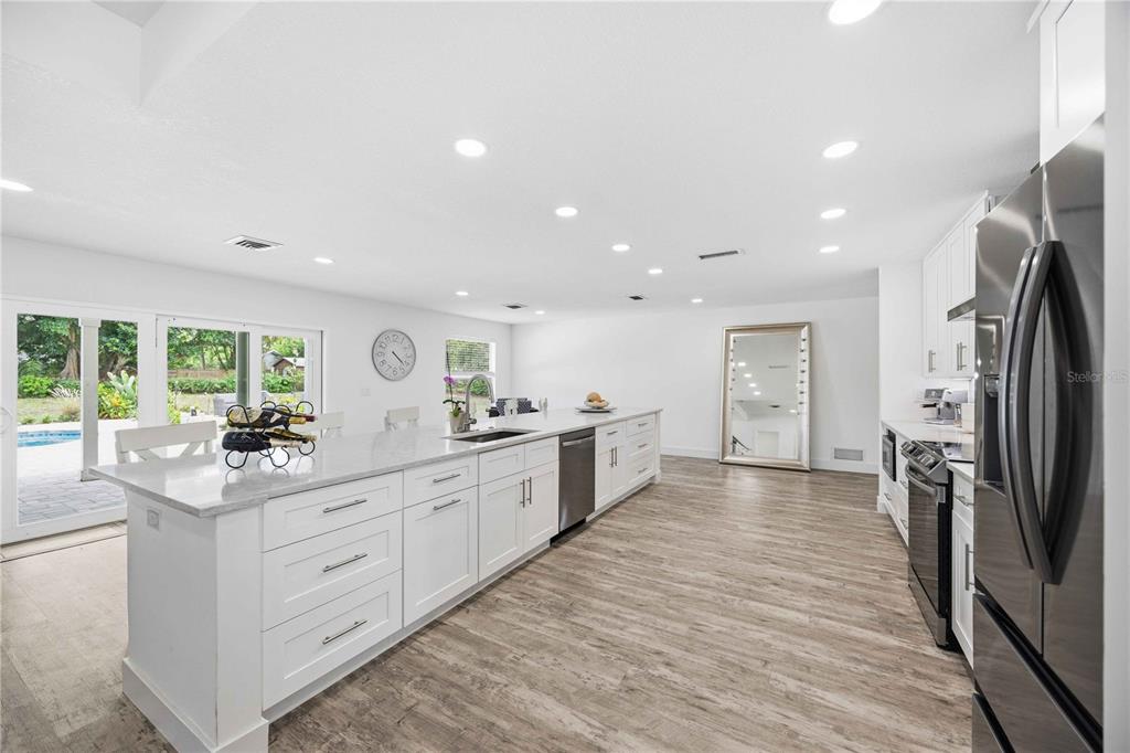 A modern kitchen features white cabinetry, a long island with a sink, and wood-look flooring — 1707 BELVIDERE ROAD, ENGLEWOOD, FL