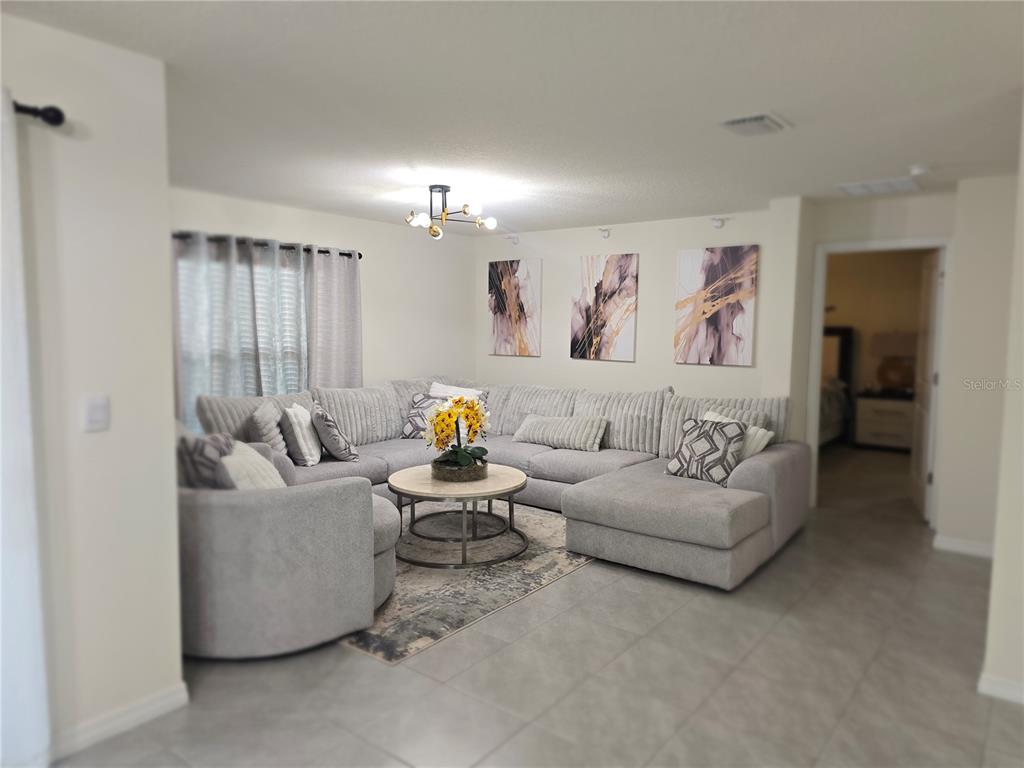 A living room features a large gray sectional sofa, a round coffee table, and wall art — 16706 SUNBURST LAKE STREET, WIMAUMA, FL