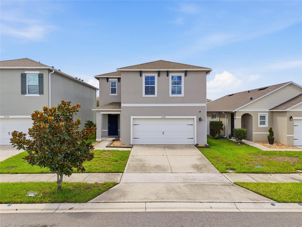 A two-story suburban house with a gray exterior, white garage door, and a front lawn — 6724 HUNTLEIGH HAMMOCK ROAD, HARMONY, FL
