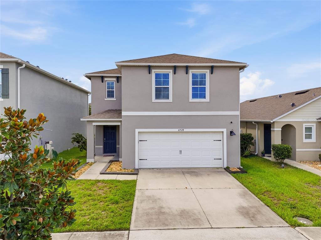 A two-story house with a gray stucco exterior, a white garage door, and a front walkway — 6724 HUNTLEIGH HAMMOCK ROAD, HARMONY, FL