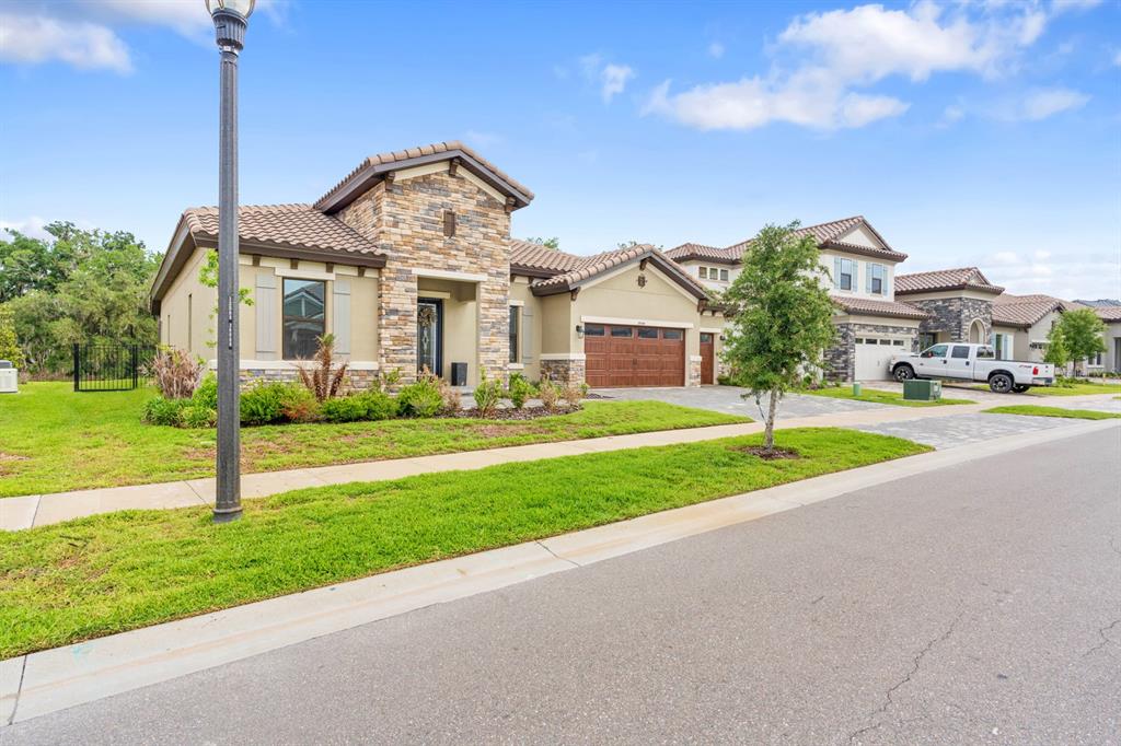 A single-story house with a stone facade, tile roof, and attached garage sits on a street — 14544 SWISS BRIDGE DRIVE, LITHIA, FL