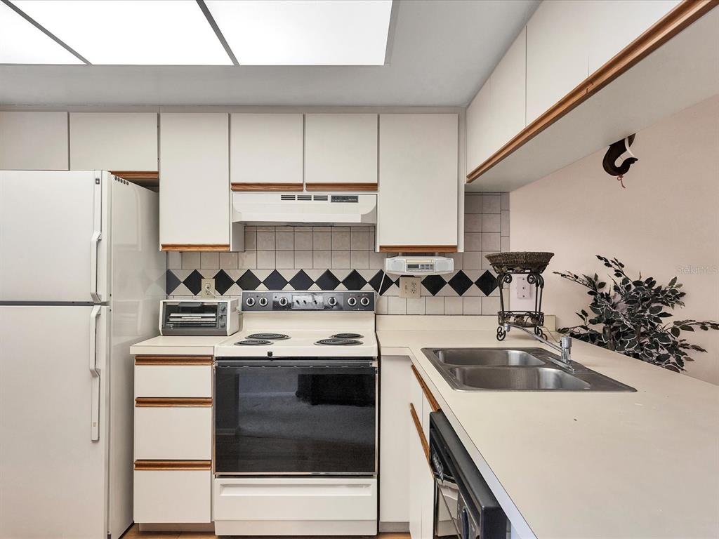 A kitchen features white cabinets, a white stove, a double sink, and a tiled backsplash — 7794 EAGLE CREEK DRIVE UNIT 7794, SARASOTA, FL