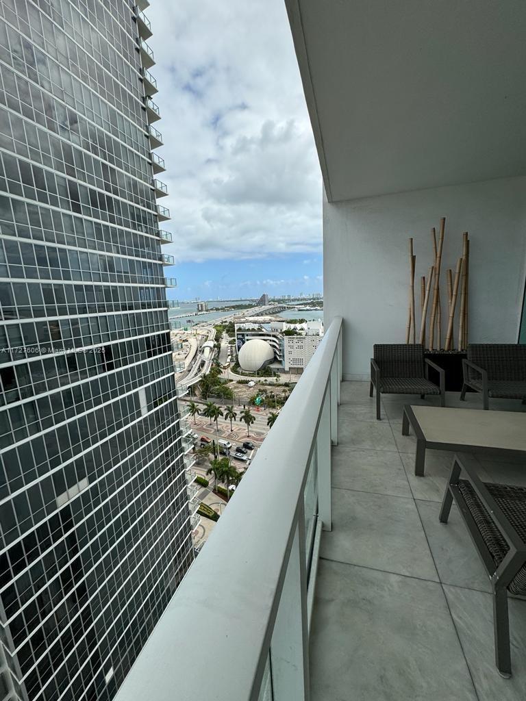 A balcony with outdoor furniture overlooks a city skyline, a bridge, and a large spherical building — 1040 Biscayne Blvd # 1505, Miami FL 33132, MIAMI, FL
