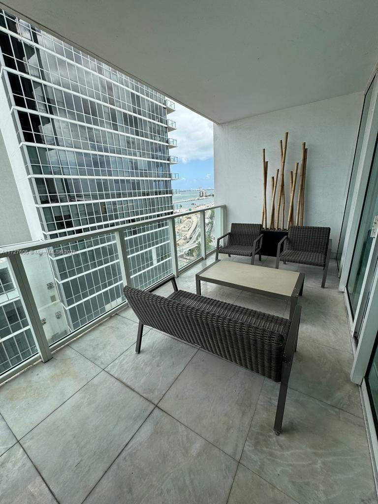 A balcony with outdoor furniture overlooks a neighboring high-rise building and a distant waterfront view — 1040 Biscayne Blvd # 1505, Miami FL 33132, MIAMI, FL