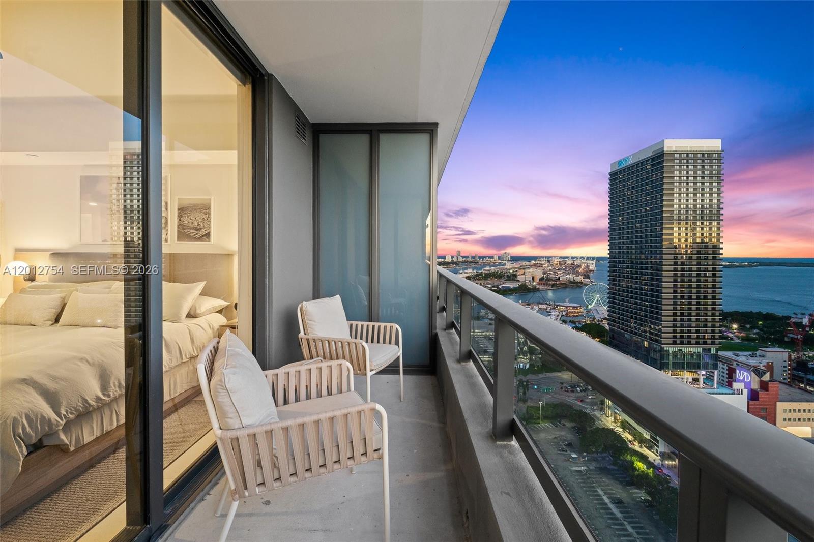 A balcony with two chairs overlooks a city skyline, a harbor, and a sunset — 601 NE 1st Ave # 3210, Miami FL 33132, MIAMI, FL