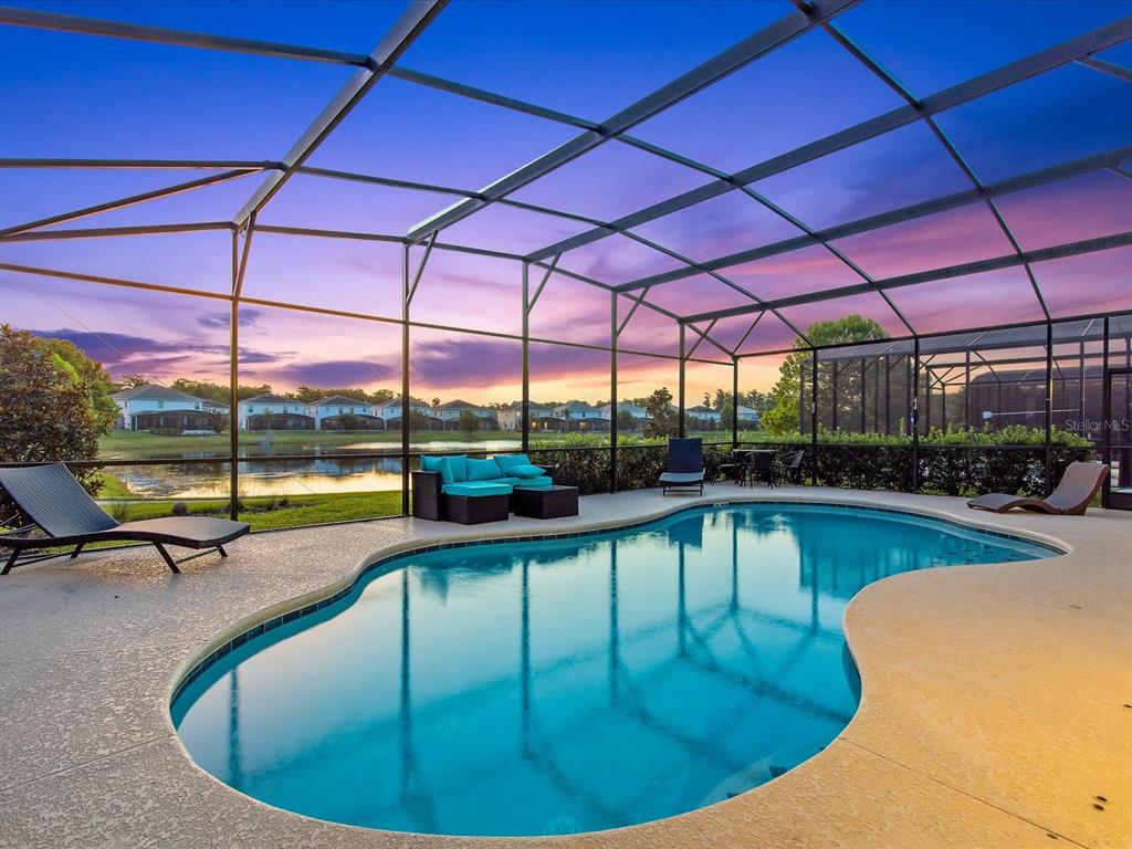 A screened-in swimming pool patio overlooks a lake and residential homes at sunset — 210 BALLO DRIVE, KISSIMMEE, FL