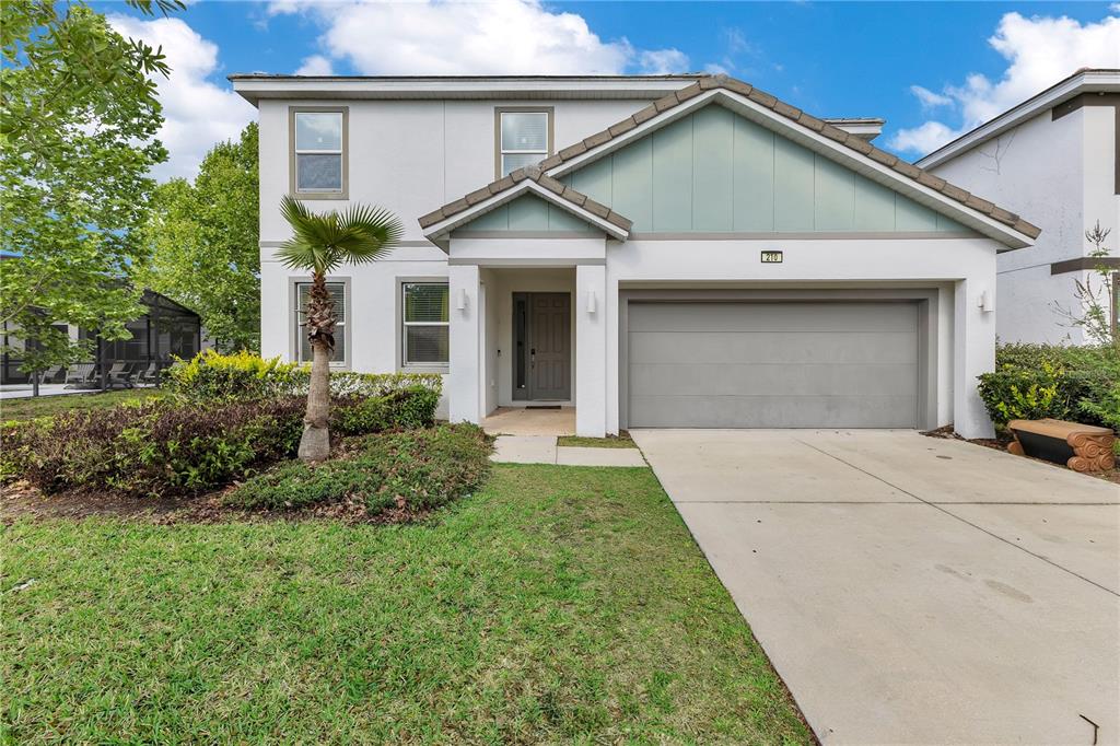 A two-story house with a white stucco exterior, a gray garage door, and a palm tree — 210 BALLO DRIVE, KISSIMMEE, FL