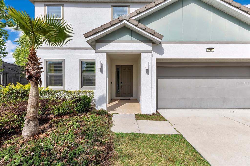 A two-story house exterior features a gray garage, a front entrance, and a palm tree — 210 BALLO DRIVE, KISSIMMEE, FL