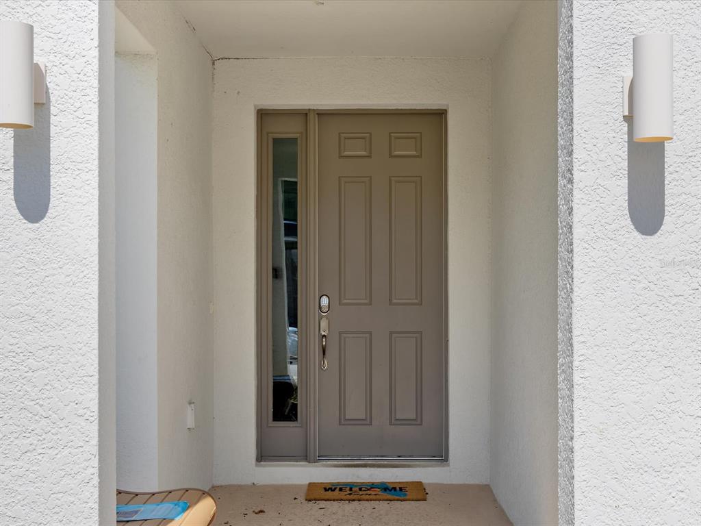 A taupe front door with a side window is framed by white walls and sconces — 210 BALLO DRIVE, KISSIMMEE, FL