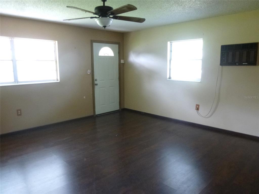 An empty room features dark wood-look flooring, beige walls, a ceiling fan, and two windows — 318 CENTRAL AVENUE, FROSTPROOF, FL