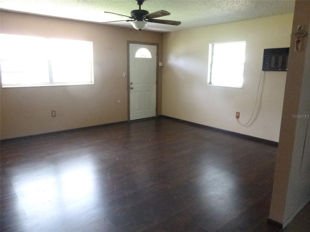 An empty living room features dark wood-look flooring, beige walls, a ceiling fan, and windows — 318 CENTRAL AVENUE, FROSTPROOF, FL