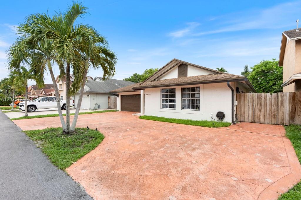 A single-story house with a stamped concrete driveway, a palm tree, and a wooden fence — 19080 NW 77th Ct, Hialeah FL 33015, HIALEAH, FL