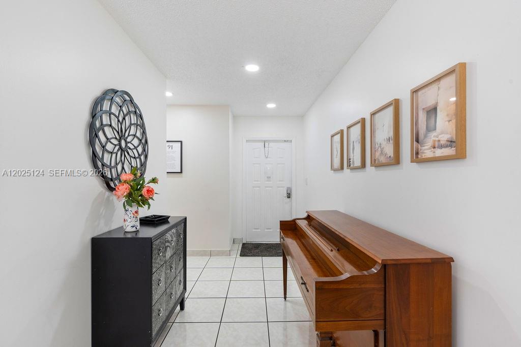 An entryway features a black chest, a wooden piano, and wall art on tiled floors — 19080 NW 77th Ct, Hialeah FL 33015, HIALEAH, FL