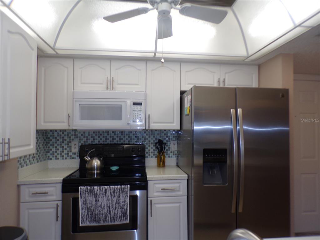 A kitchen features white cabinets, stainless steel appliances, and a blue mosaic tile backsplash — 4016 OAKVIEW DRIVE UNIT J8, PUNTA GORDA, FL
