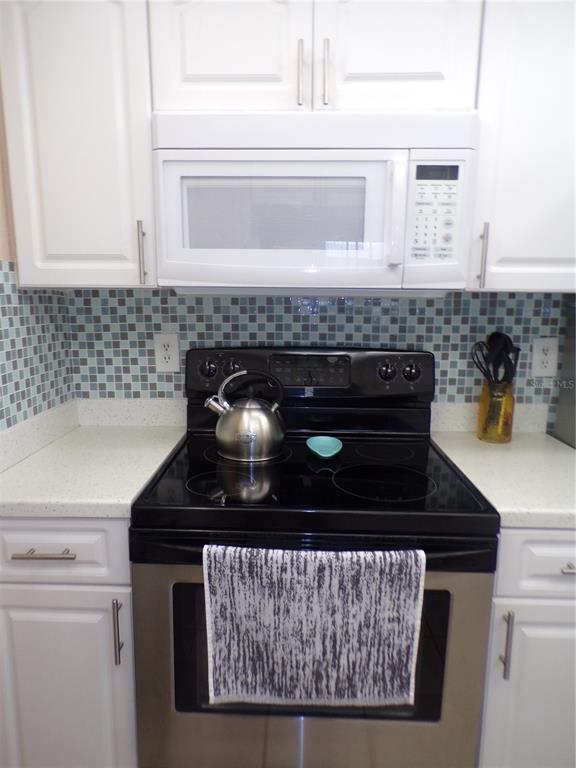 A kitchen features white cabinets, a black electric stove, and a blue mosaic tile backsplash — 4016 OAKVIEW DRIVE UNIT J8, PUNTA GORDA, FL