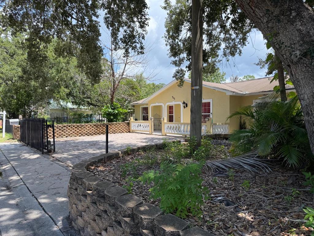 A yellow house with a paved front yard and a stone retaining wall — 711 S EMORY AVENUE, KISSIMMEE, FL