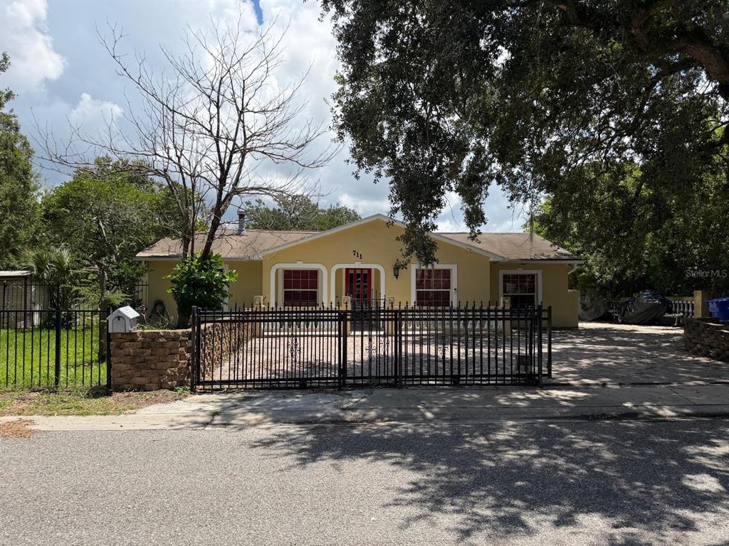 A single-story yellow house features a black metal fence and a paved front yard — 711 S EMORY AVENUE, KISSIMMEE, FL