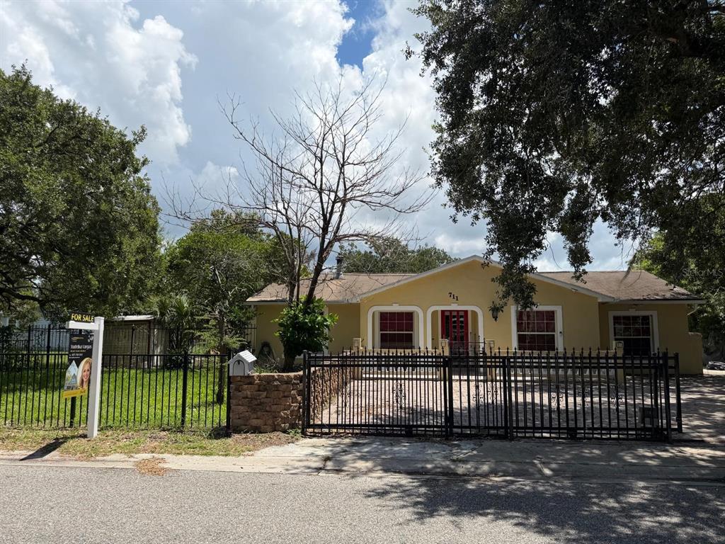 A yellow single-story house with a black metal fence and gate sits behind a paved driveway — 711 S EMORY AVENUE, KISSIMMEE, FL