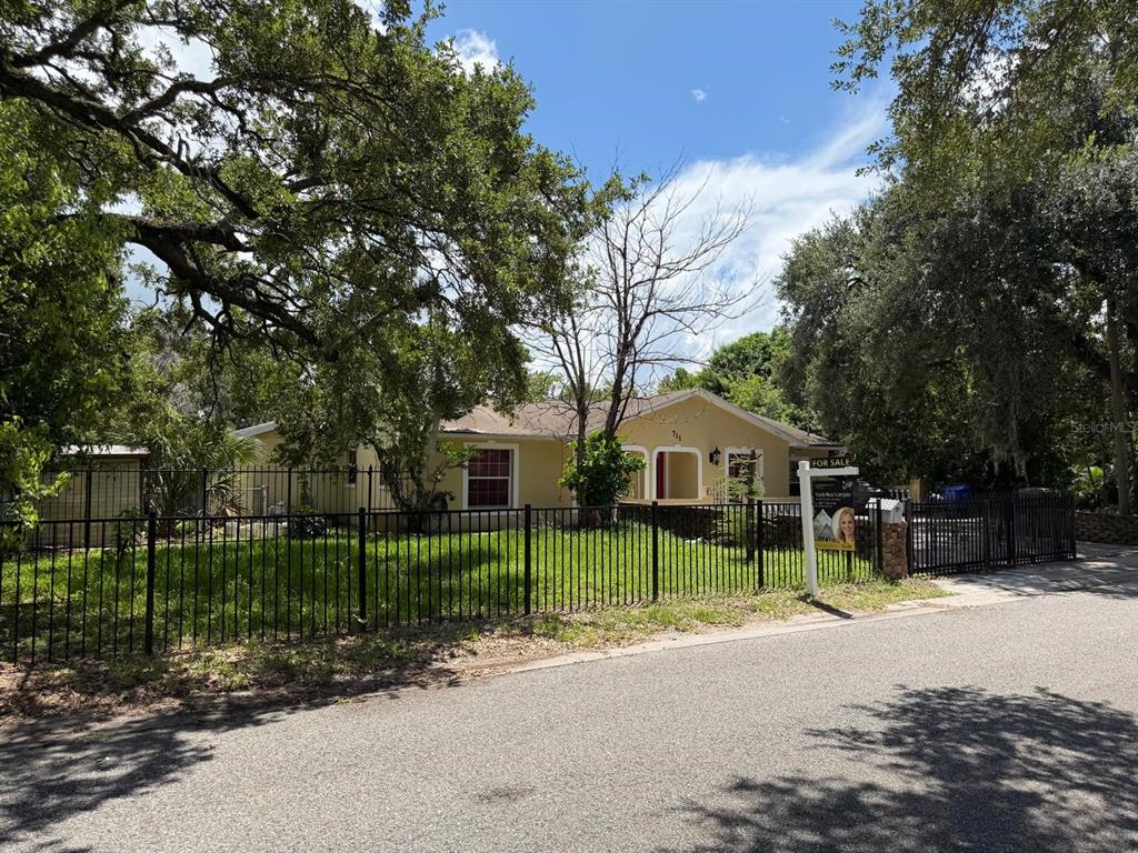A single-story house with a fenced yard and mature trees stands behind a for-sale sign — 711 S EMORY AVENUE, KISSIMMEE, FL