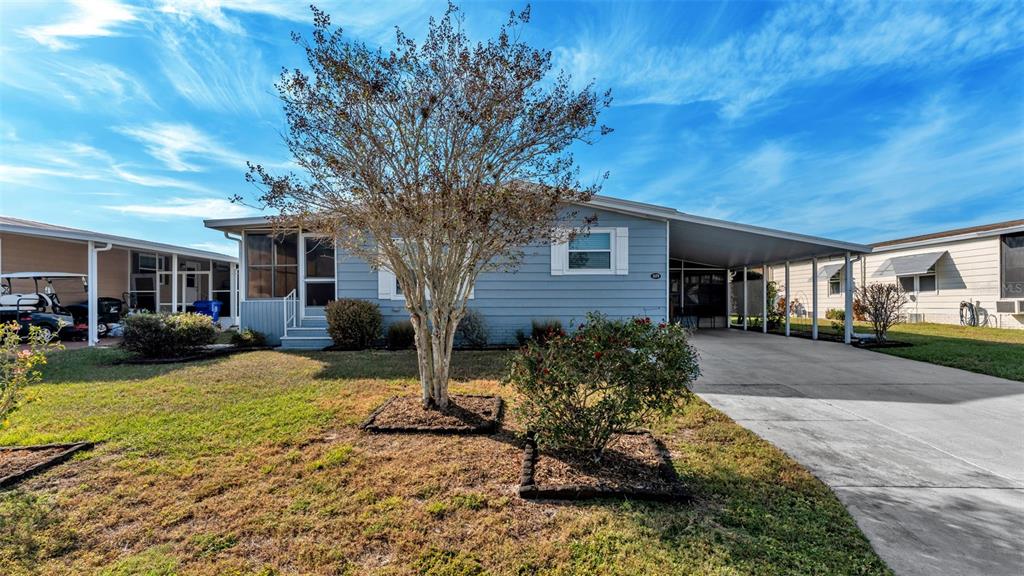 A light blue single-story house features a front carport, a large tree, and a lawn — 5079 LODGEWOOD DRIVE, LAKELAND, FL