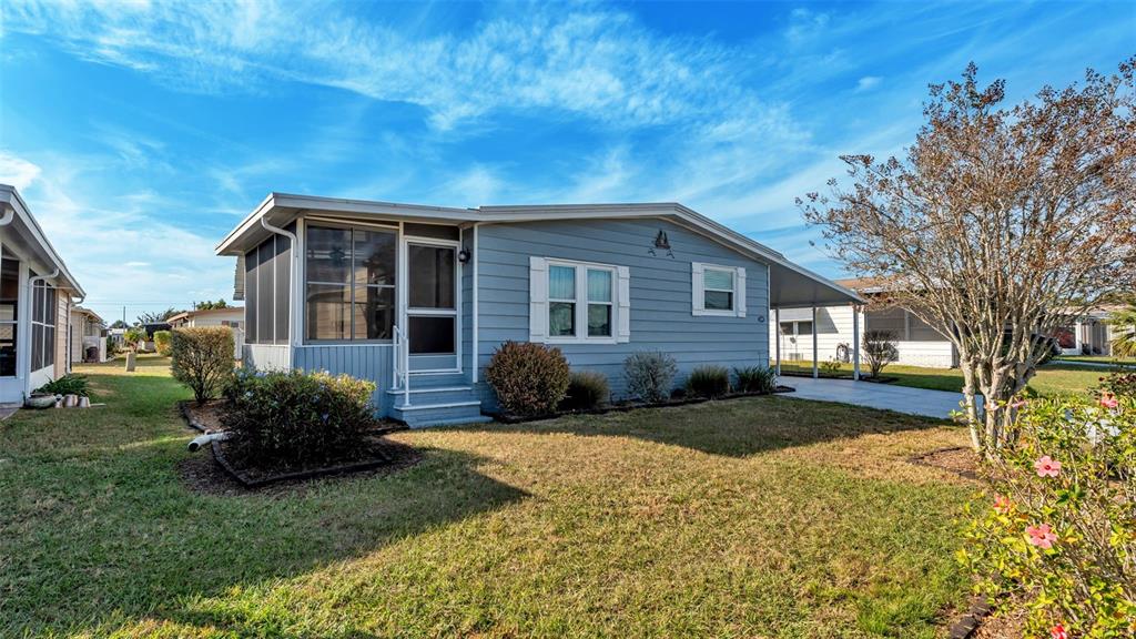 A light blue single-story house features a screened-in porch, a carport, and a grassy yard — 5079 LODGEWOOD DRIVE, LAKELAND, FL