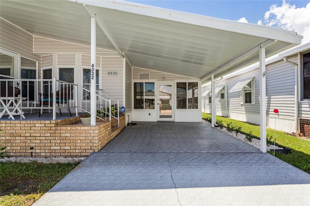 A manufactured home features a covered carport, a brick-walled porch, and light-colored vinyl siding — 4332 CHERRYWOOD STREET, WINTER HAVEN, FL