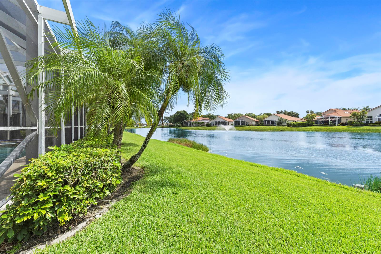 A palm tree stands on a grassy lawn beside a lake with a water fountain — 637 Masters Way, Palm Beach Gardens FL 33418, PALM BEACH GARDENS, FL