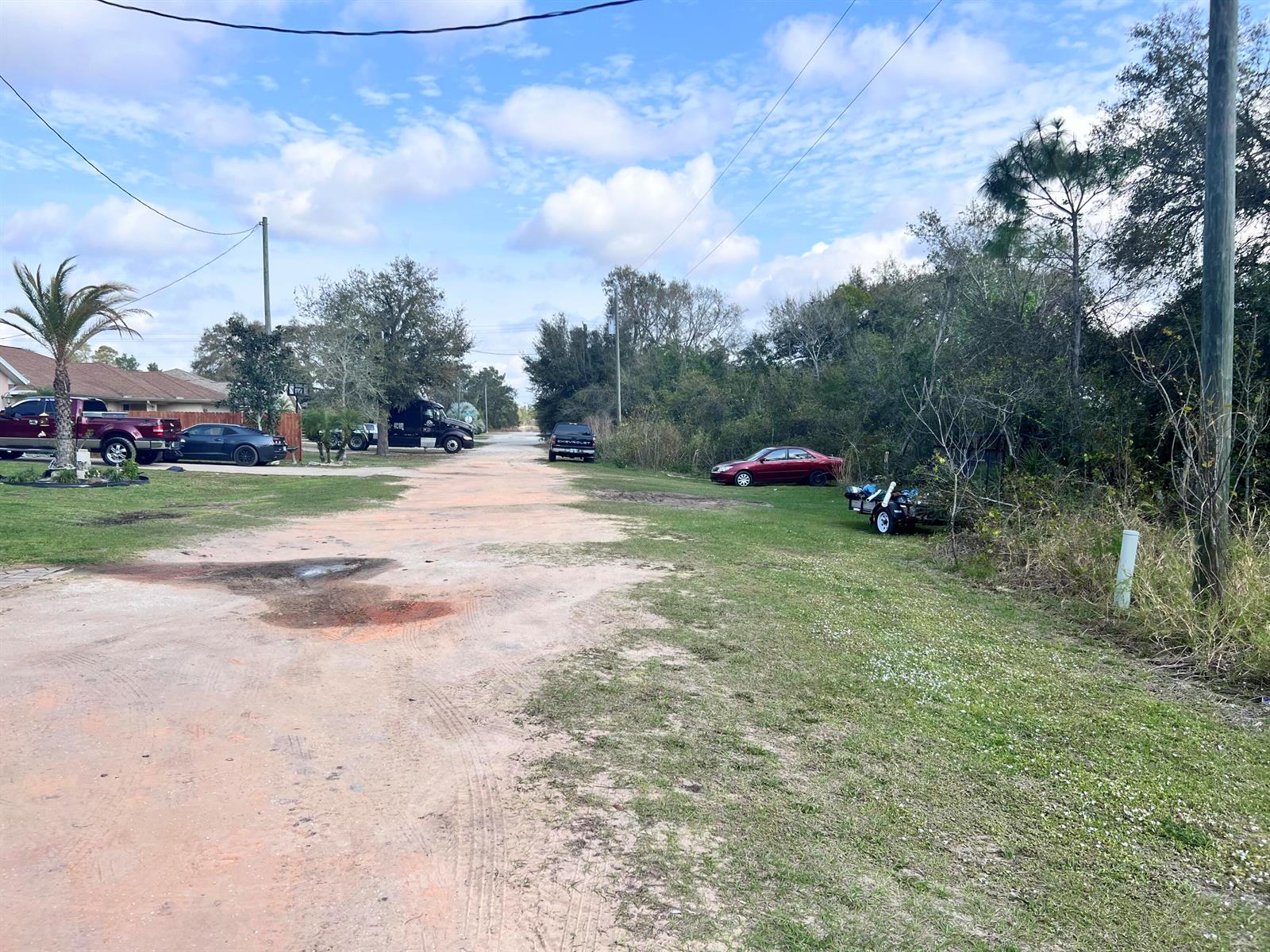 A dirt road leads through a residential area with parked cars and scattered trees — 13528 Hull Street, FL 33875, FL
