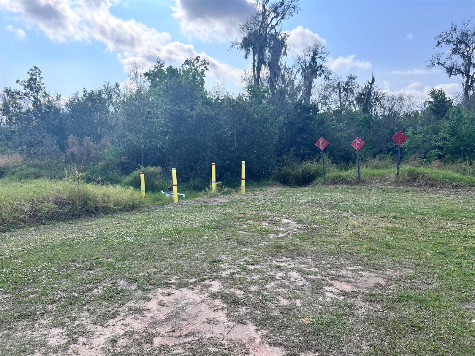 A grassy field features four yellow bollards and three red diamond-shaped signs near a treeline — 13528 Hull Street, FL 33875, FL