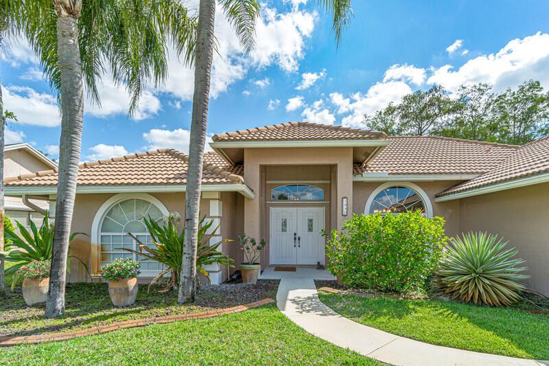 The exterior of a single-story house features a tiled roof, palm trees, and landscaping — 1840 Hollyhock Road, Wellington FL 33414, WELLINGTON, FL
