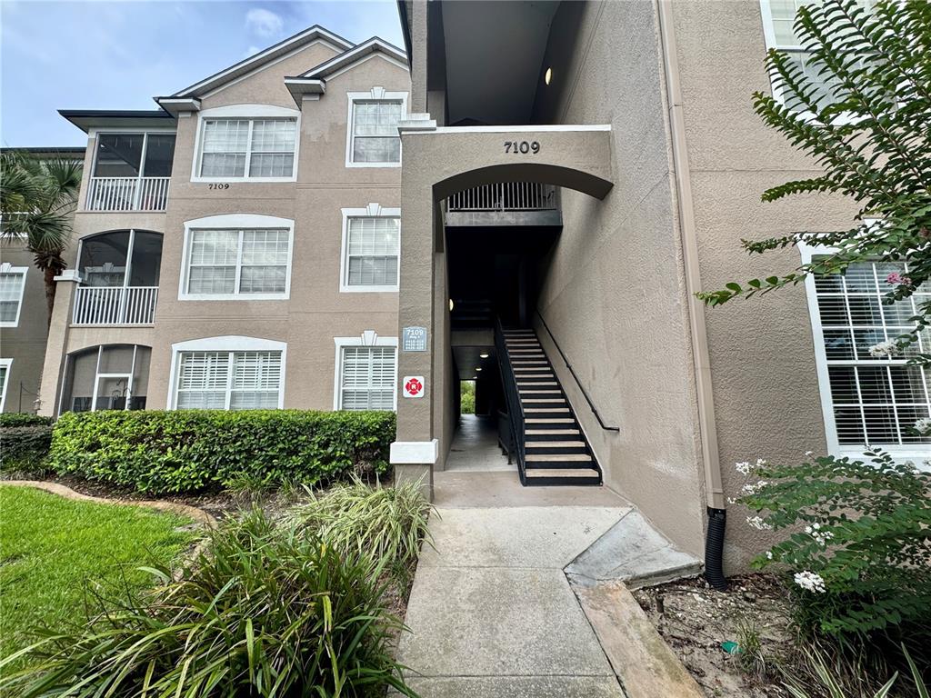 The exterior of a multi-story apartment building features a central staircase leading to upper units — 7109 YACHT BASIN AVENUE UNIT 418, ORLANDO, FL