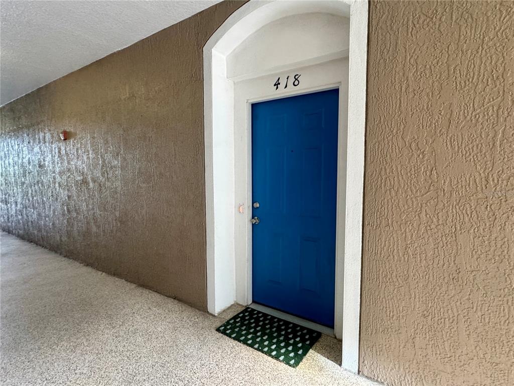 A bright blue front door with the number 418 is set in a textured tan wall — 7109 YACHT BASIN AVENUE UNIT 418, ORLANDO, FL