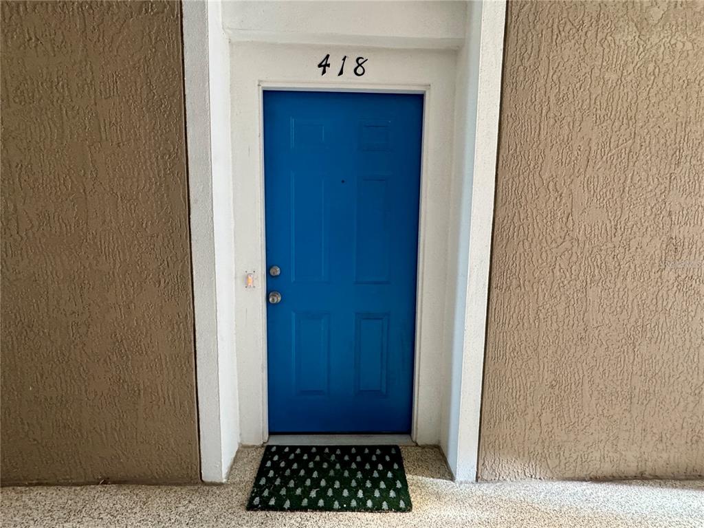 A bright blue front door with the number 418 above it sits in a stucco wall — 7109 YACHT BASIN AVENUE UNIT 418, ORLANDO, FL