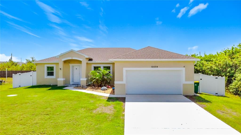 A single-story house with a beige exterior, a two-car garage, and a white fence — 10024 LEBANON DR, PORT CHARLOTTE, FL