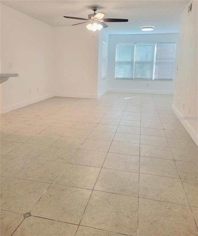 An empty room with light-colored tile flooring, a ceiling fan, and large windows with blinds — 4528 COMMANDER DRIVE UNIT 2011, ORLANDO, FL