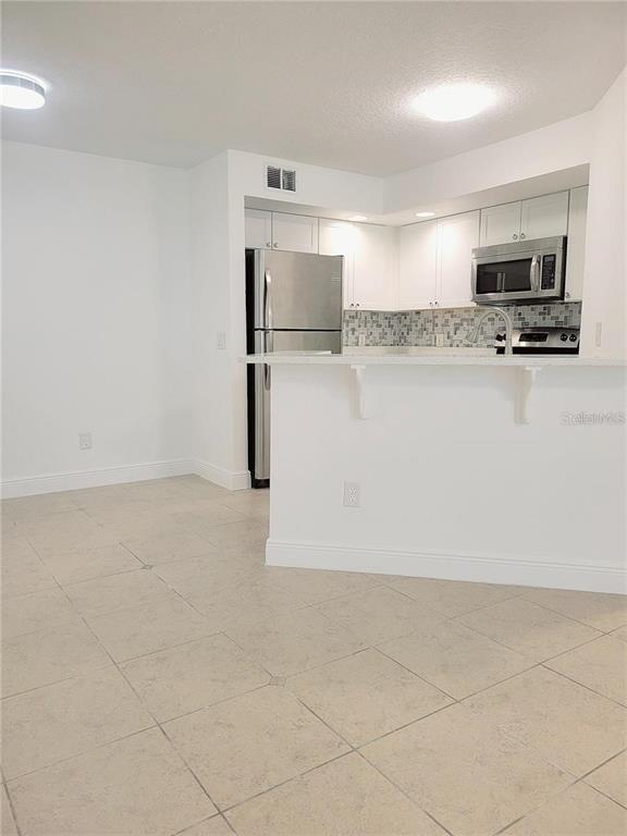 A kitchen with white cabinets, stainless steel appliances, and a breakfast bar overlooks a tiled area — 4528 COMMANDER DRIVE UNIT 2011, ORLANDO, FL